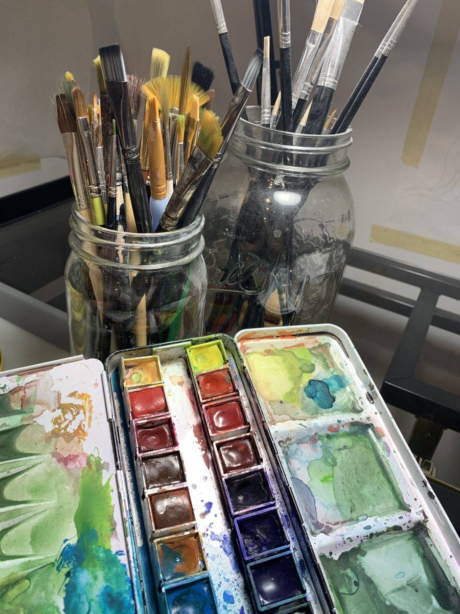 Two mason jars filled with the artist's paintbrushes, with a palette tin in front