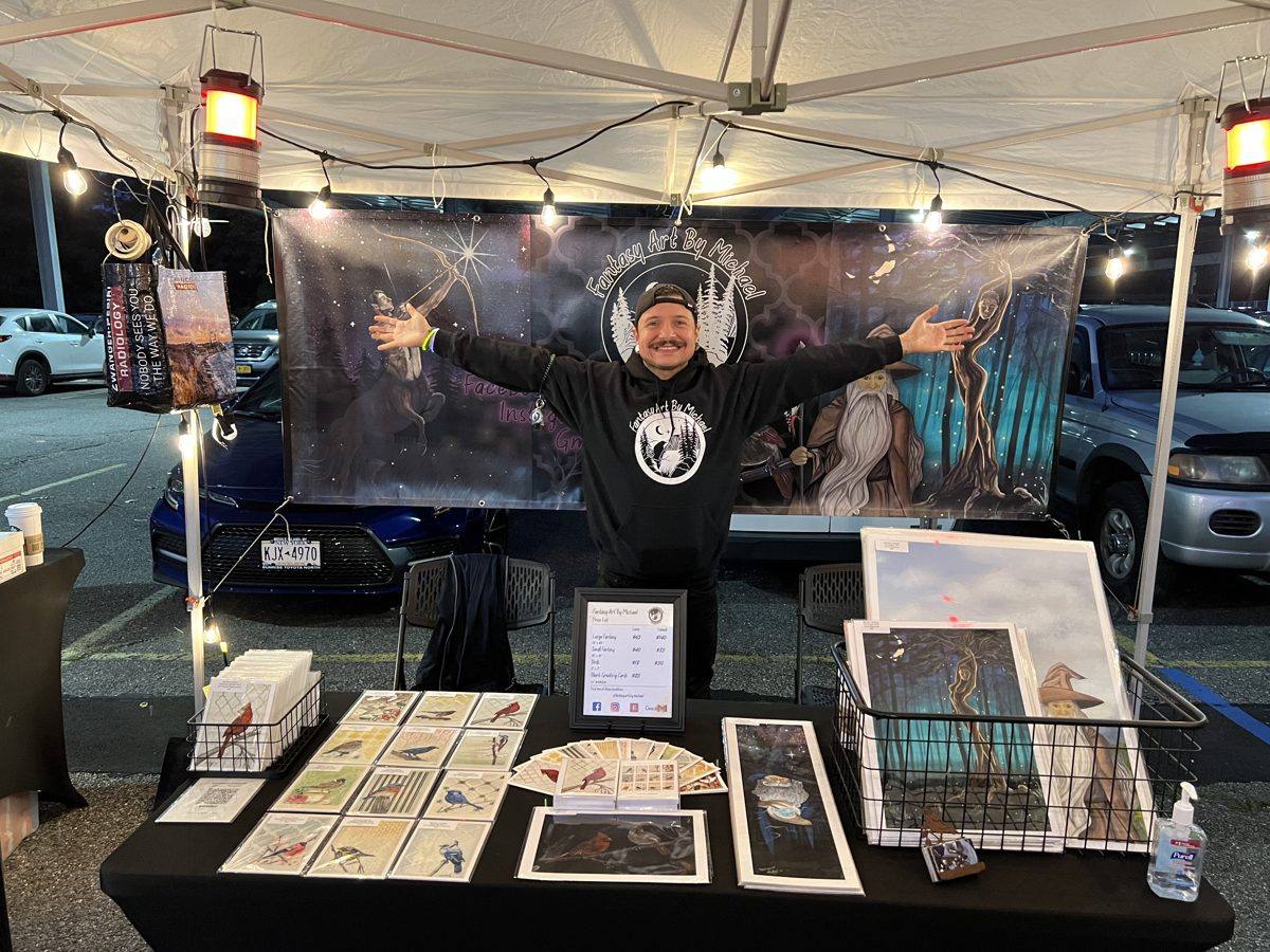 Michael Lombardi standing with arms wide at his Fantasy Art by Michael market booth