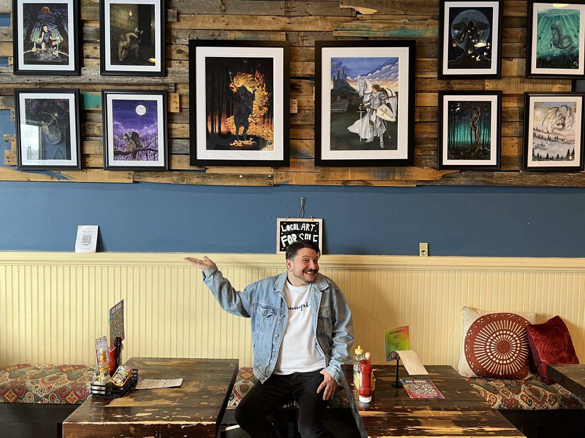 Michael Lombardi seated in front of a wall of his framed fantasy paintings